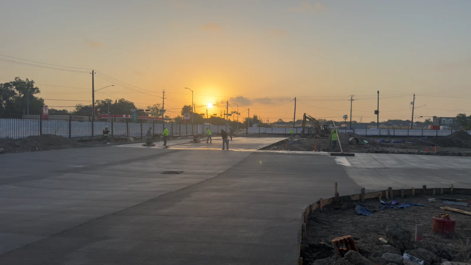 Crew power-troweling a freshly poured commercial concrete slab at sunrise in Houston